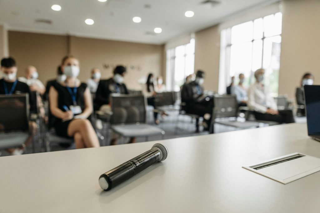 A business conference room setting with masked participants and a microphone in the foreground.